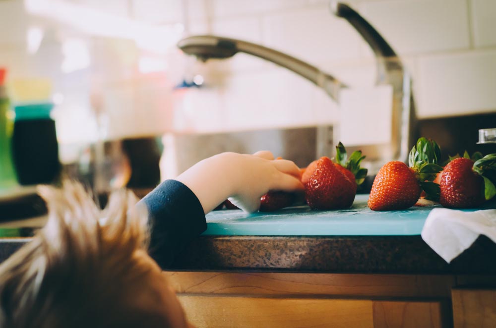 Child taking a strawberry from a countertop